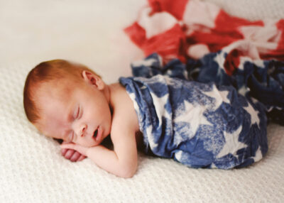 Photo of IVF rainbow baby Rourke wrapped up in an American flag | Dallas IVF | Frisco, TX